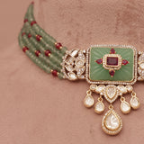 Decorative necklace with green stone and red beads on a brown velvet stand