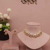 Gold necklace and earrings on display with a vase of flowers and 'BIBI' branding in the background.