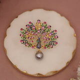 Decorative brooch with gemstones on a round white plate with gold rim against a pink background