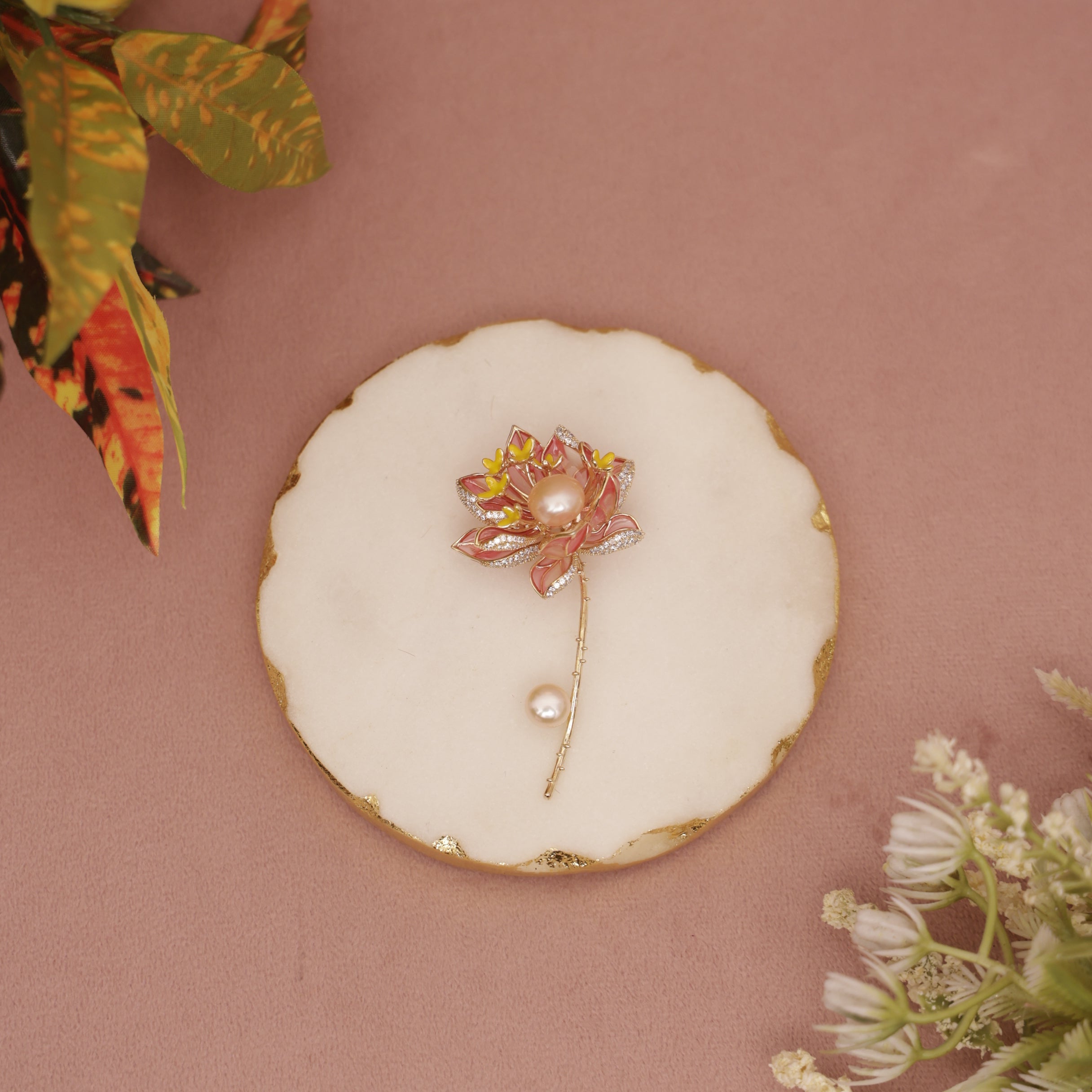 Decorative brooch on a round white dish with gold rim against a pink background