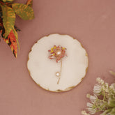 Decorative brooch on a round white dish with gold rim against a pink background