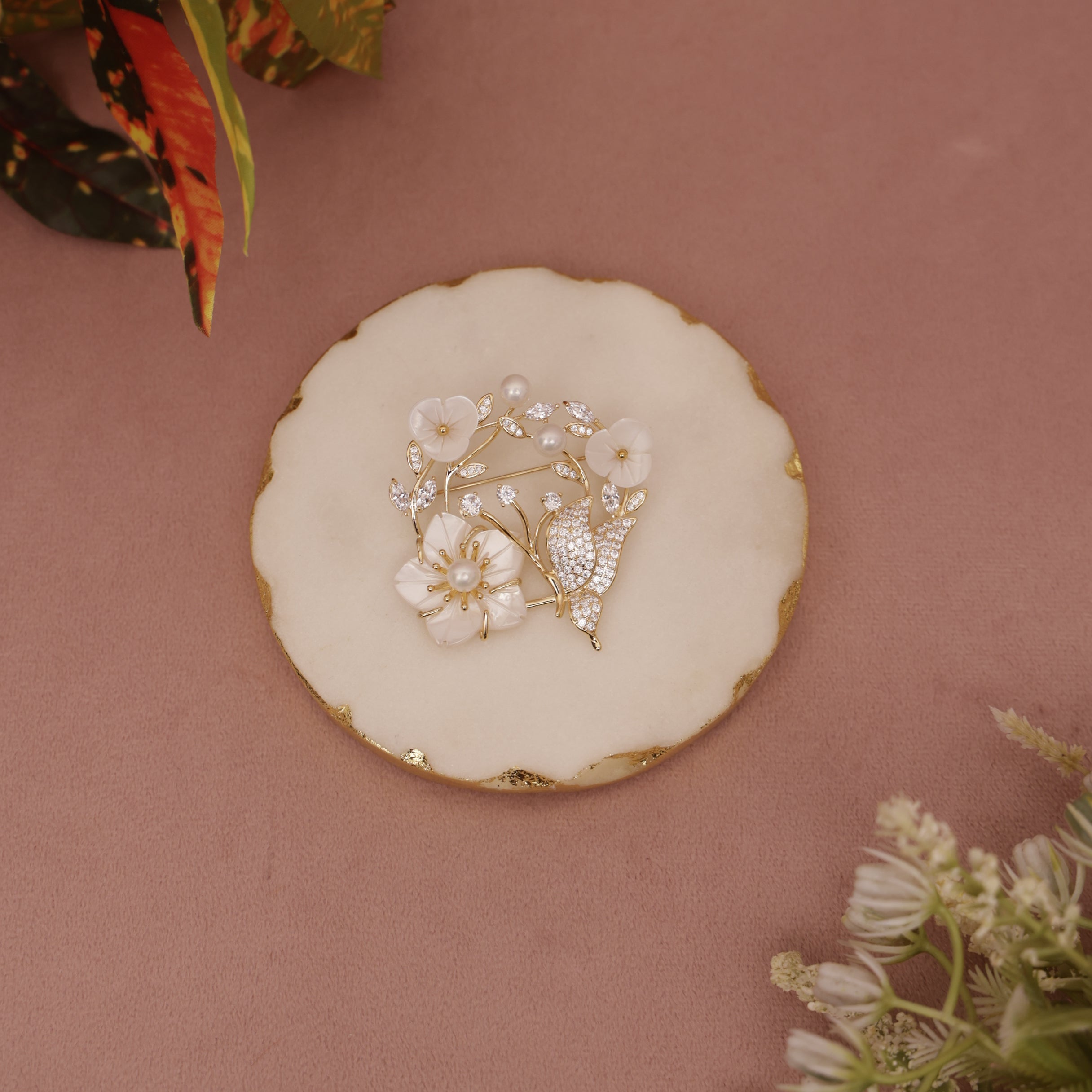 Decorative brooch with floral design on a pink surface with floral elements.