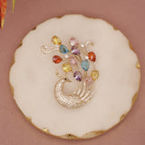 Decorative cookie with a peacock design and colorful gemstones on a pink background