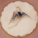 Gold and blue bird-shaped brooch on a decorative white and gold circular base