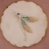 Decorative brooch with gold and green leaf design on a beige background