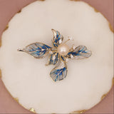 Decorative brooch with pearl and blue leaves on a white cushion