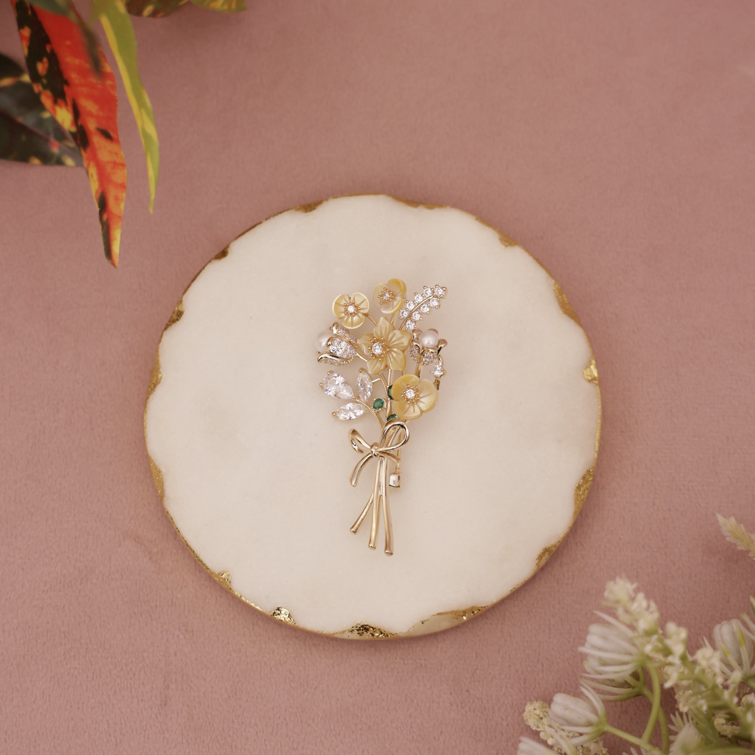 Gold floral brooch on a round white dish with a pink background