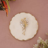 Gold floral brooch on a round white dish with a pink background