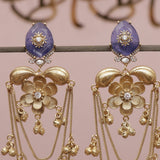 Gold earrings with floral designs and purple stones on a pink background