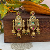 Ornate gold earrings with gemstones on a wooden box with leaves in the background