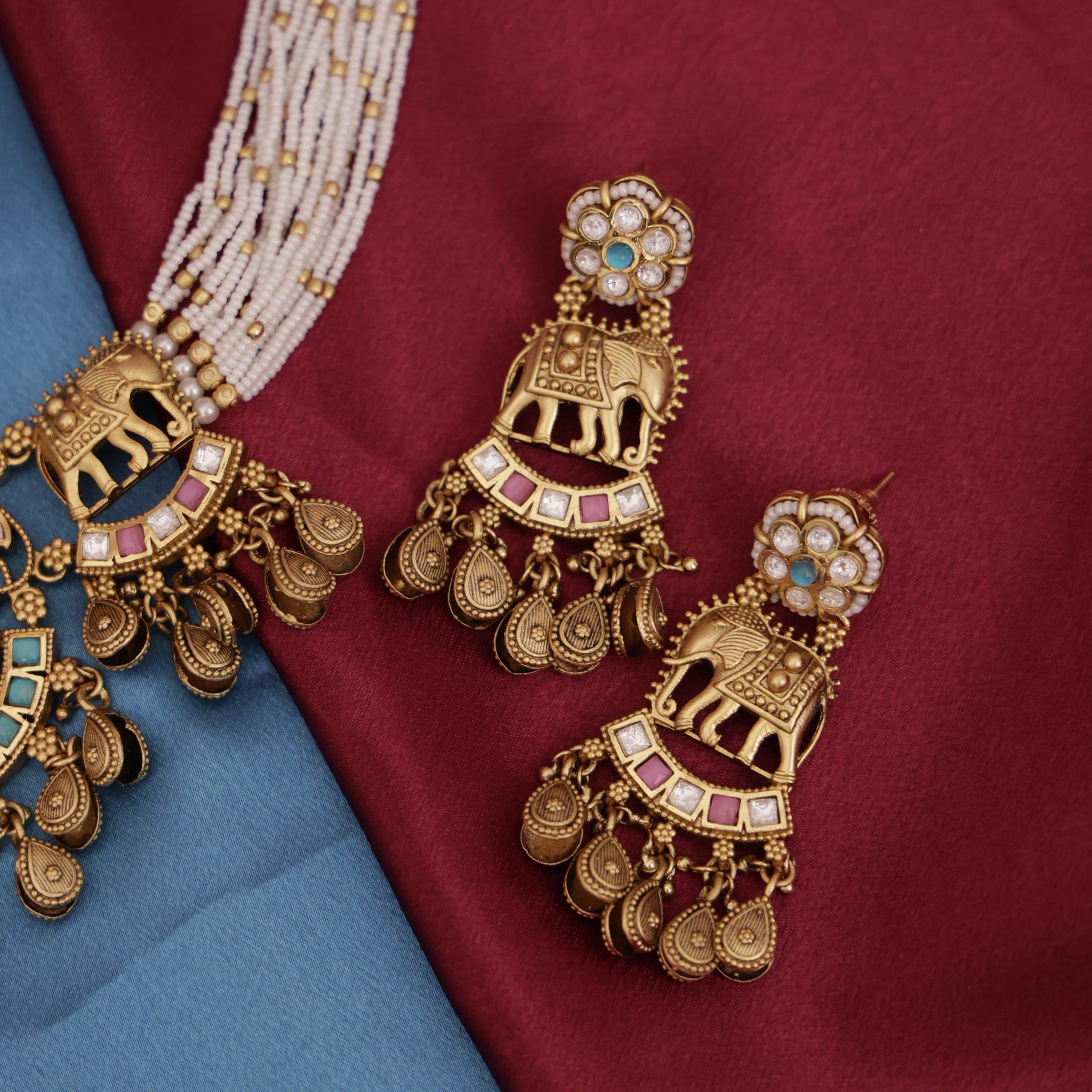 Ornate gold earrings with gemstones on a red and blue fabric background
