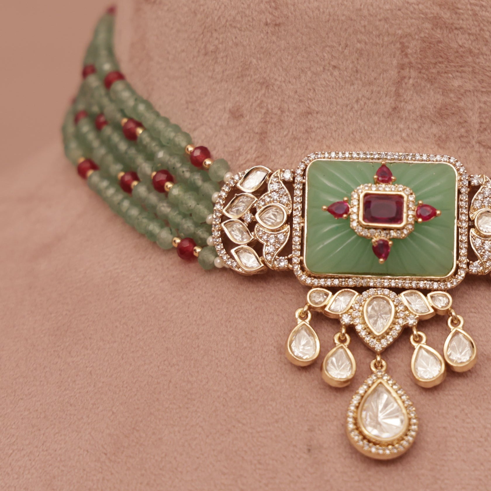 Decorative necklace with green stone and red beads on a brown velvet stand