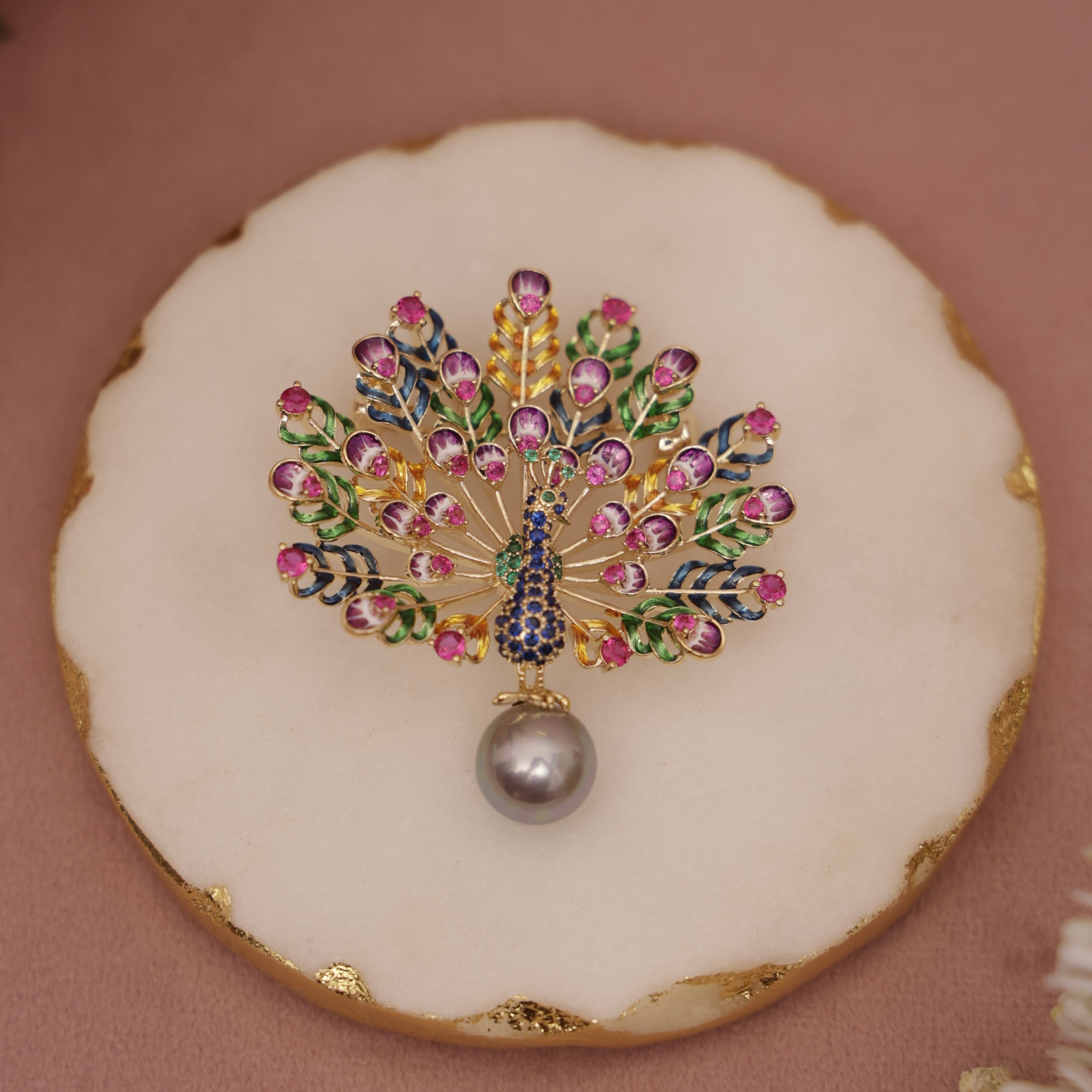 Decorative brooch with gemstones on a round white plate with gold rim against a pink background