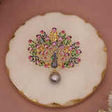 Decorative brooch with gemstones on a round white plate with gold rim against a pink background