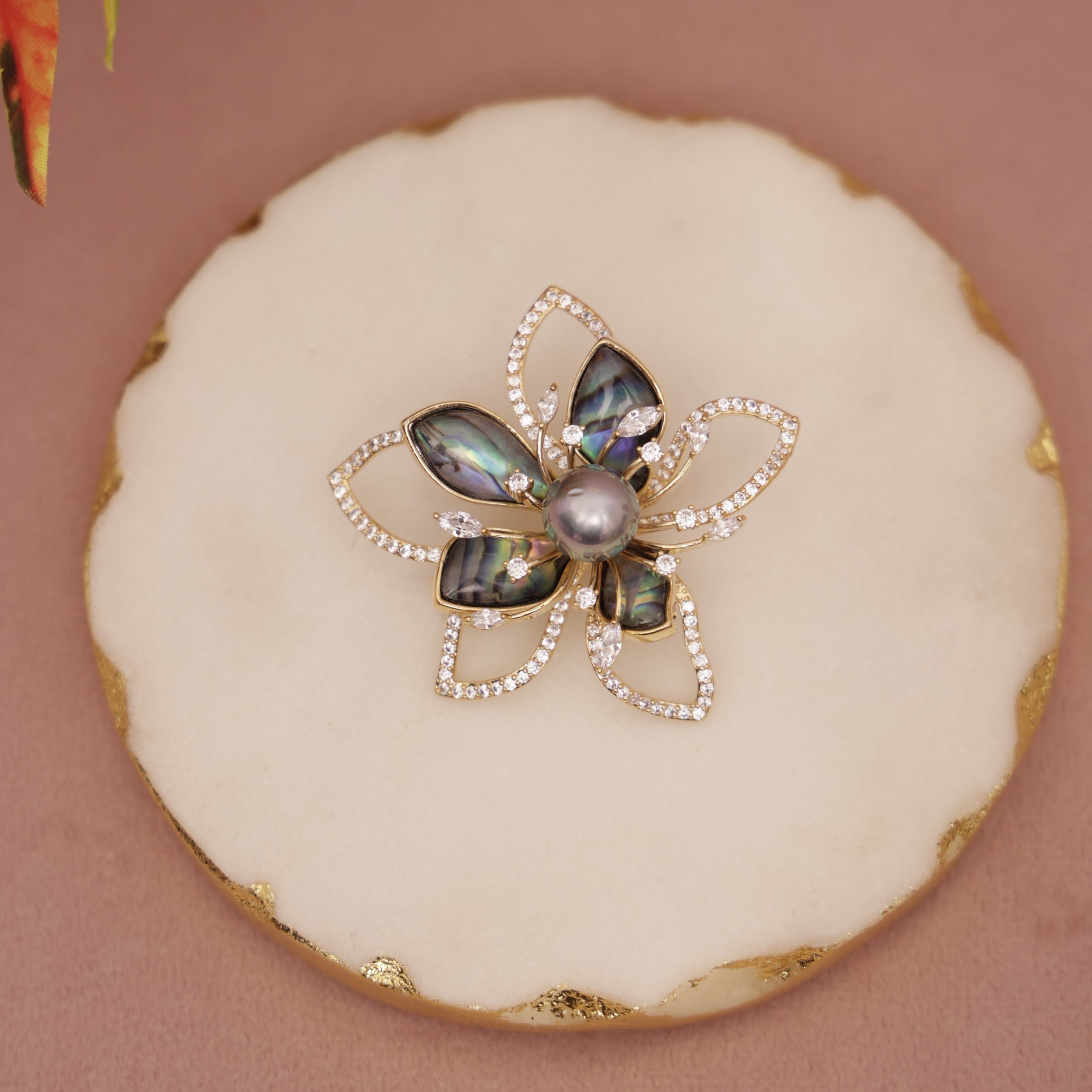 Decorative flower-shaped object with a central pearl on a round white surface.
