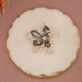 Decorative flower-shaped object with a central pearl on a round white surface.