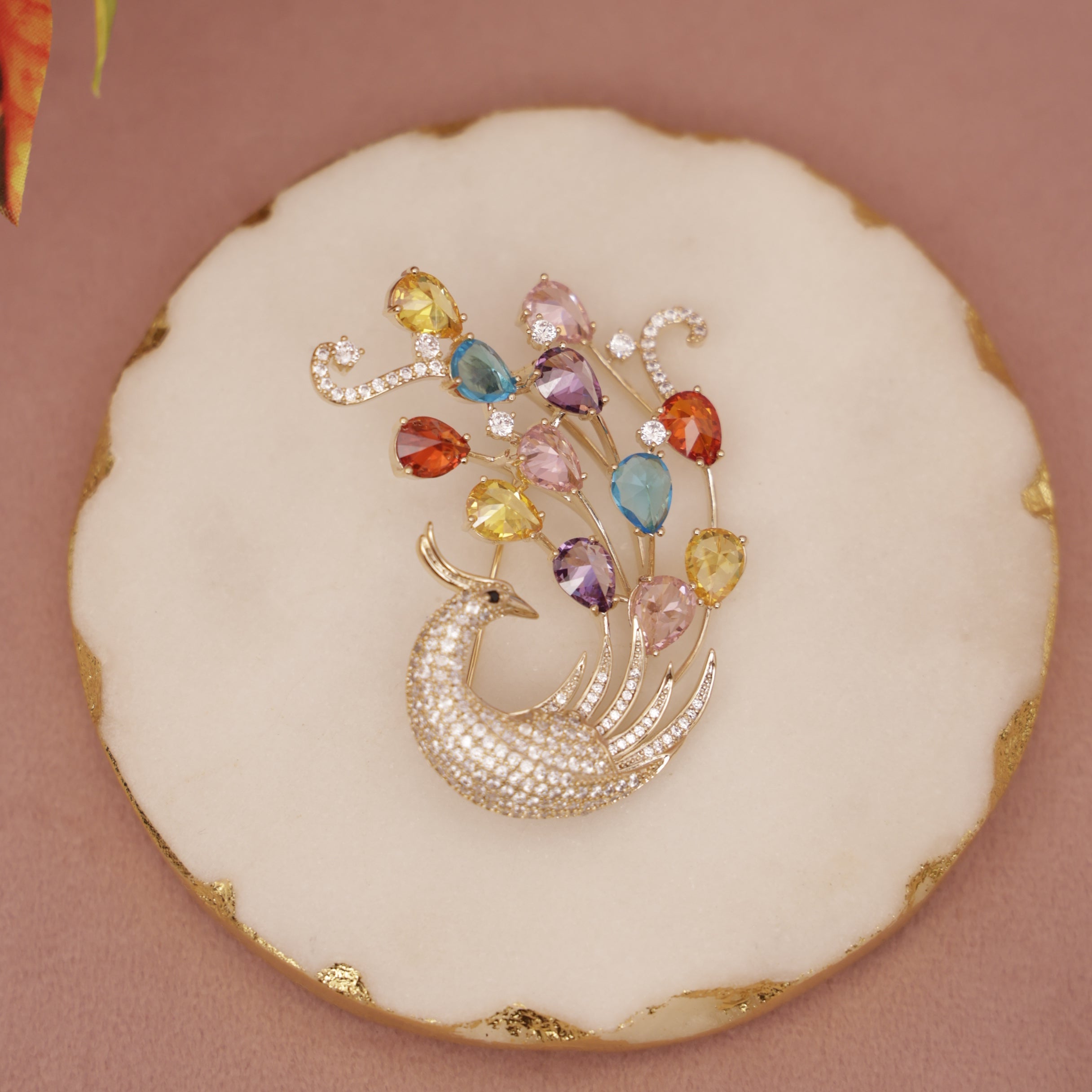 Decorative cookie with a peacock design and colorful gemstones on a pink background