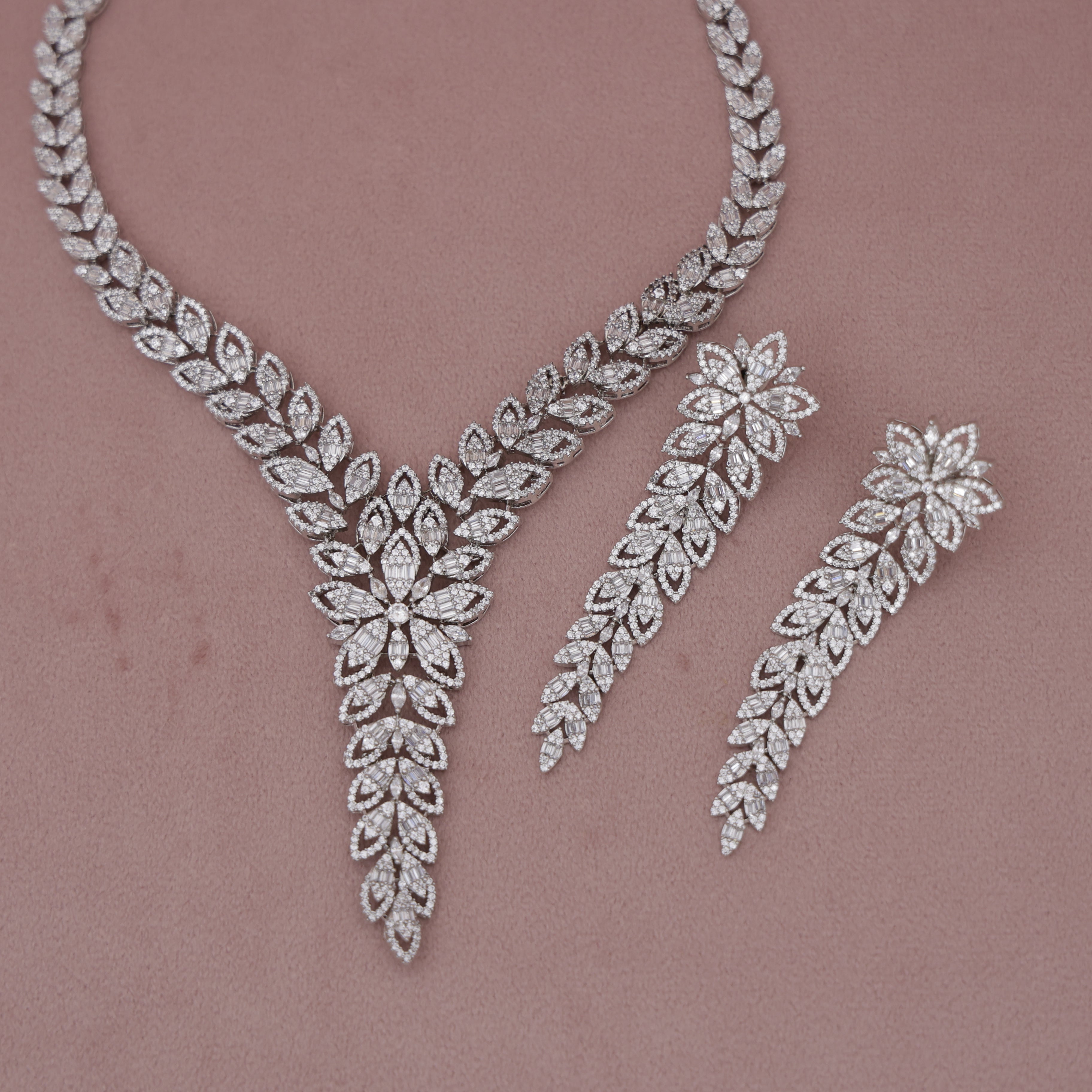 Silver necklace and earrings set on a pink background