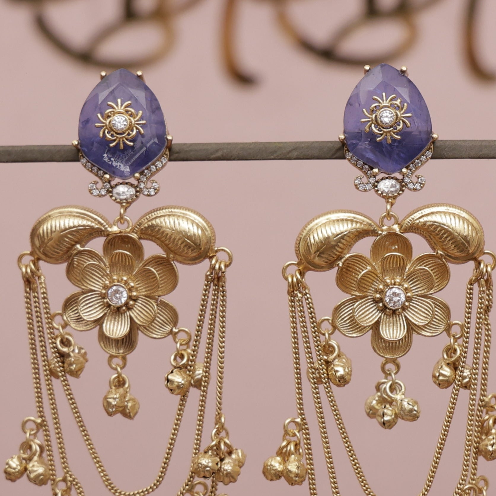 Gold earrings with floral designs and purple stones on a pink background